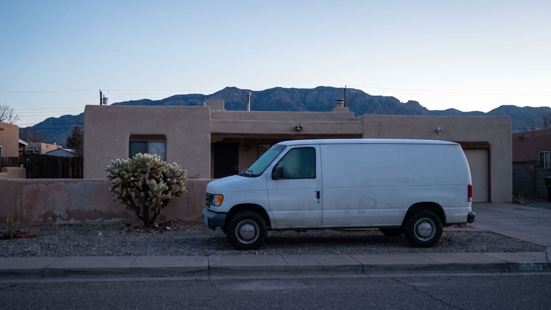 Illustration: a white cargo van on the gravel drive of a pueblo-style stucco house in Albuquerque at dusk, the Sandia mountains behind.