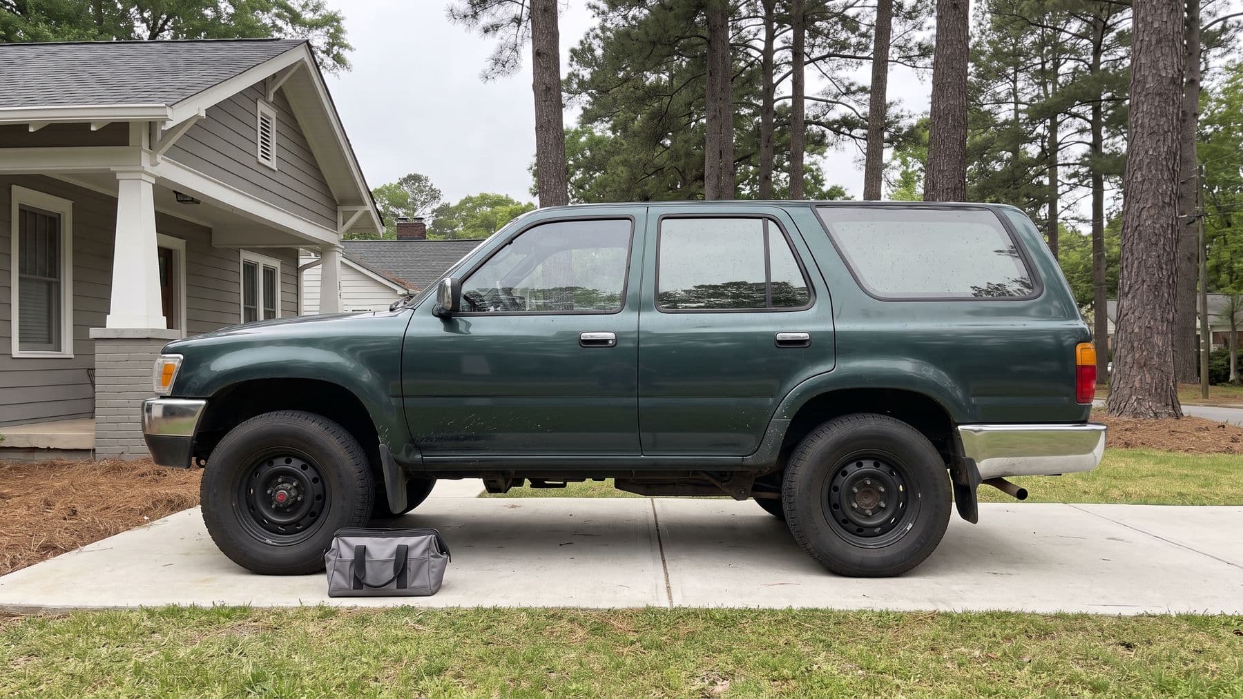 Illustration: a dark green 1990s SUV parked nose-in on the driveway of a gray craftsman house in Decatur, Georgia, pines behind.