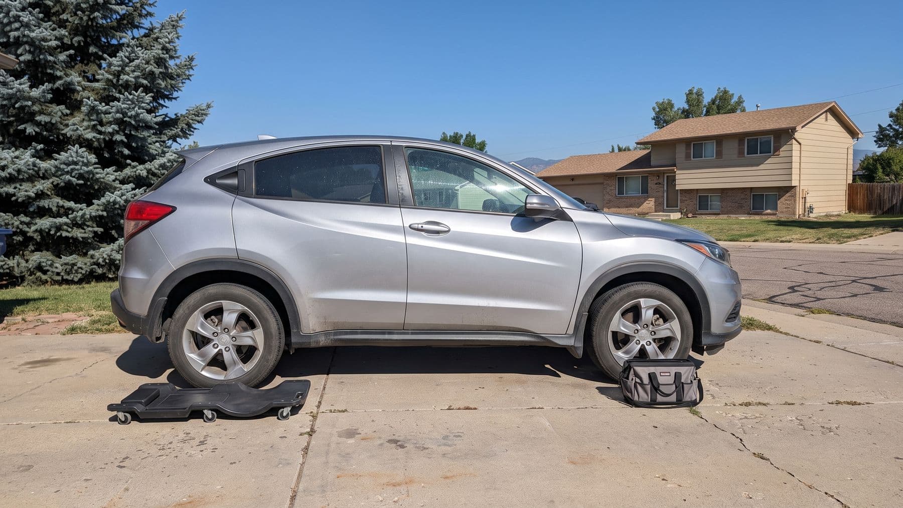 Illustration: a silver crossover parked nose-in on the driveway of a bi-level house in Lakewood, Colorado, foothills behind.
