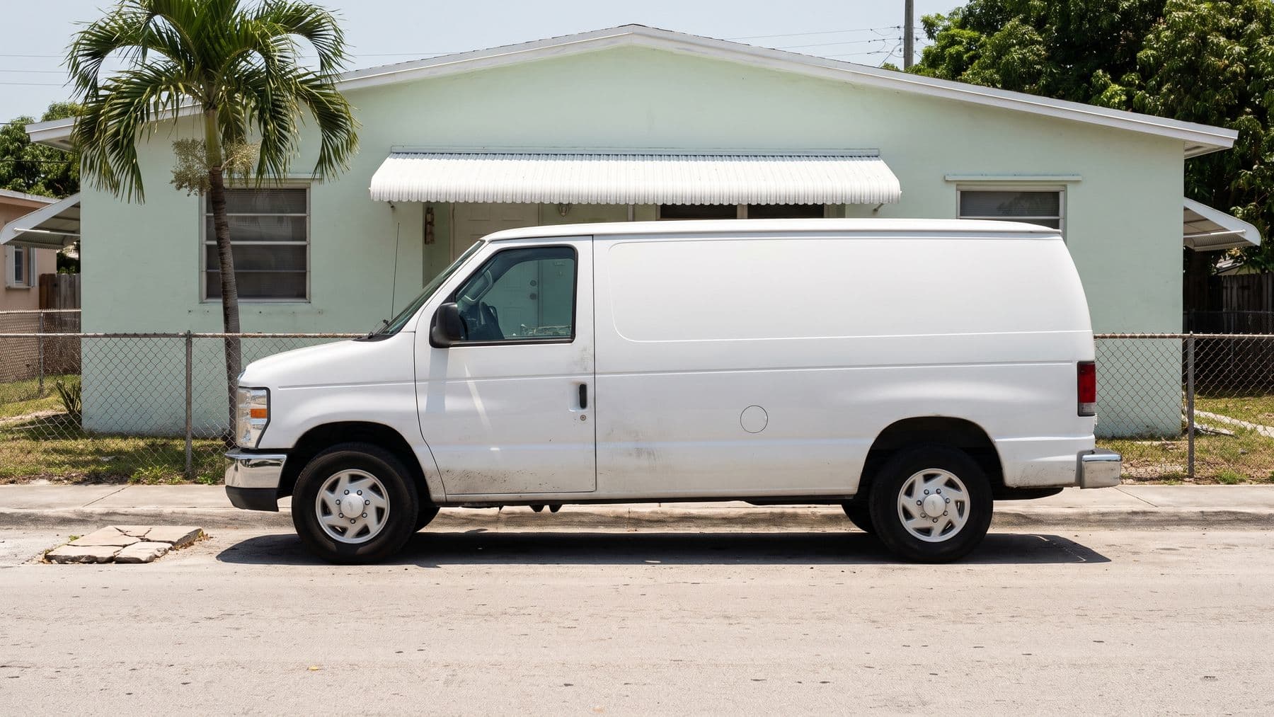 Illustration: a white cargo van parked at the curb in front of a mint stucco duplex in Hialeah, a royal palm and a chain-link fence.