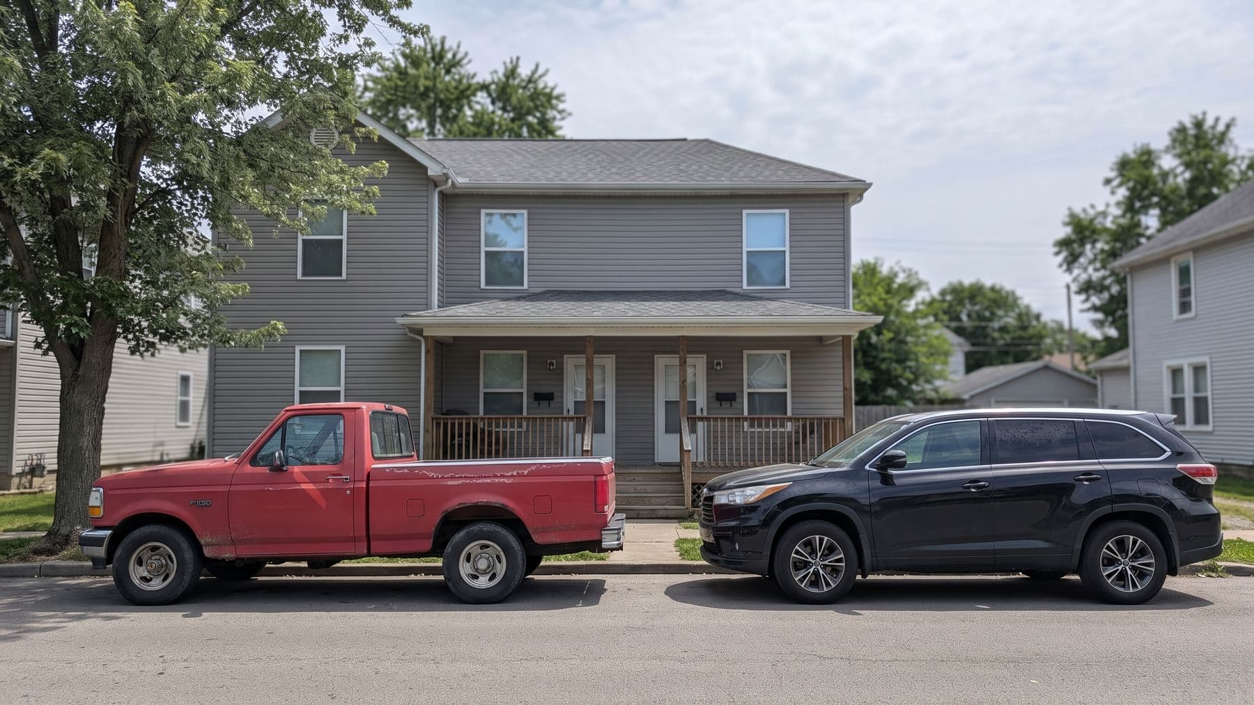 Illustration: a faded red 1990s pickup and a newer black SUV parked nose to tail at the curb of a two-family house in Columbus, Ohio.
