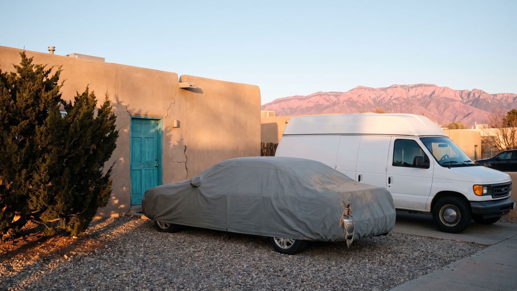 Illustration: a sedan under a gray fabric car cover on the gravel pad of a pueblo-style house in Albuquerque, the Sandia mountains behind.