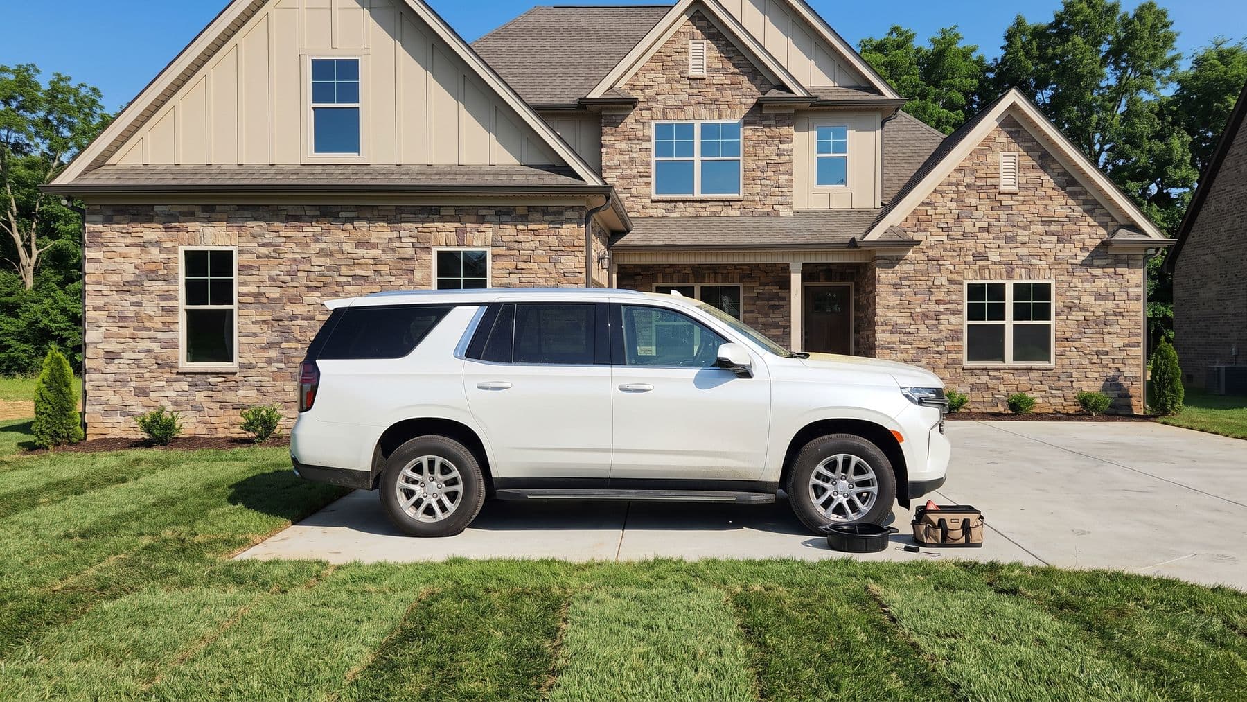 Illustration: a pearl-white full-size SUV on the driveway of a new stone-veneer house in Franklin, Tennessee, a drain pan beside it.