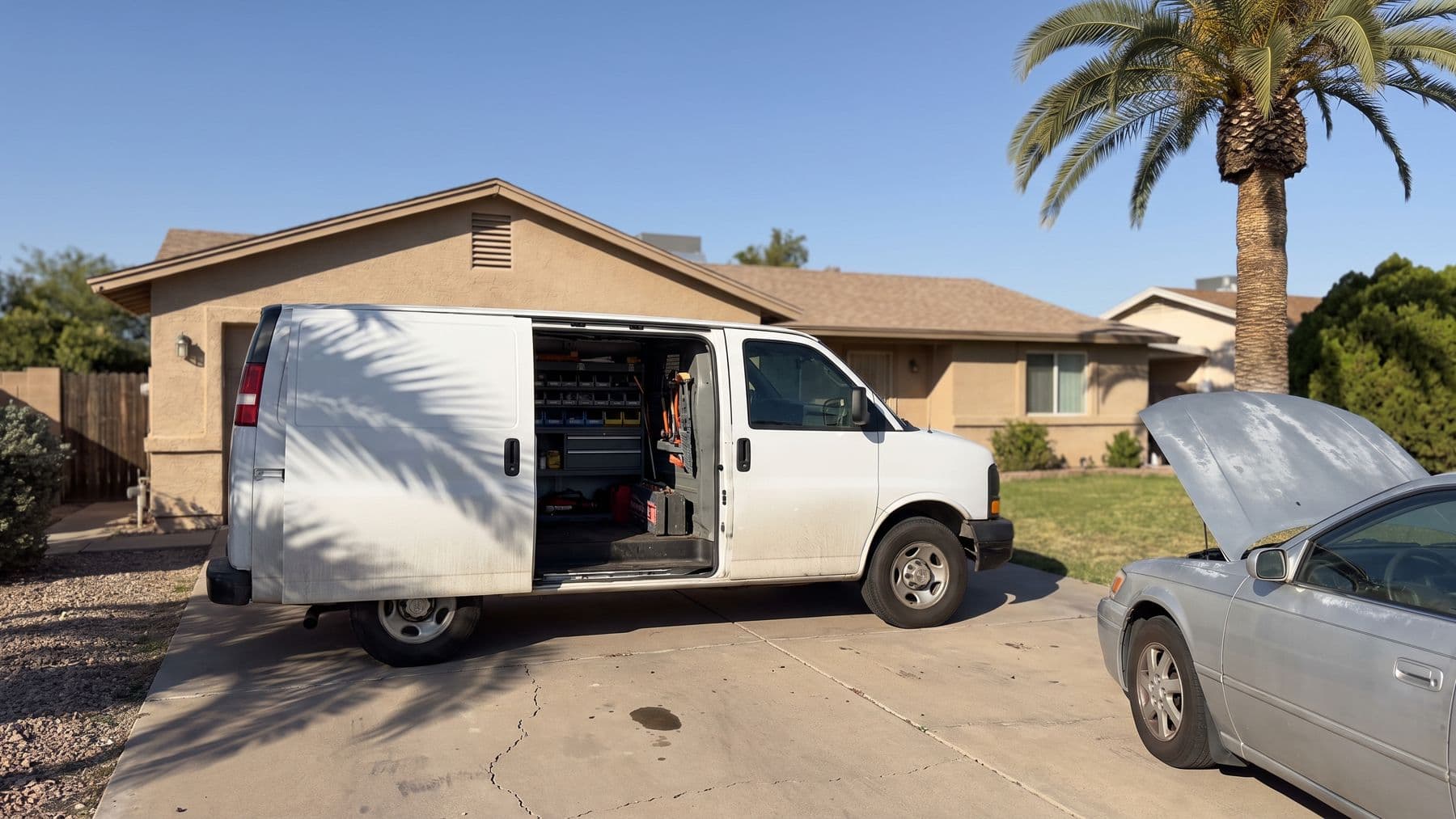 Illustration: a white cargo van with its sliding door open in the driveway of a tan stucco ranch in a Phoenix suburb, a palm shadow across the concrete.