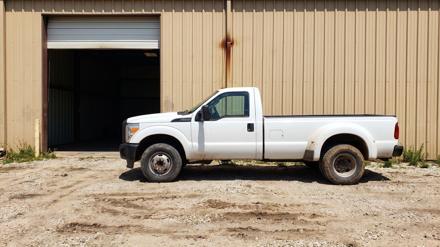 Illustration: a white dually pickup parked along a steel-sided shop outside Wichita, one roll-up door raised, a rutted gravel lot.
