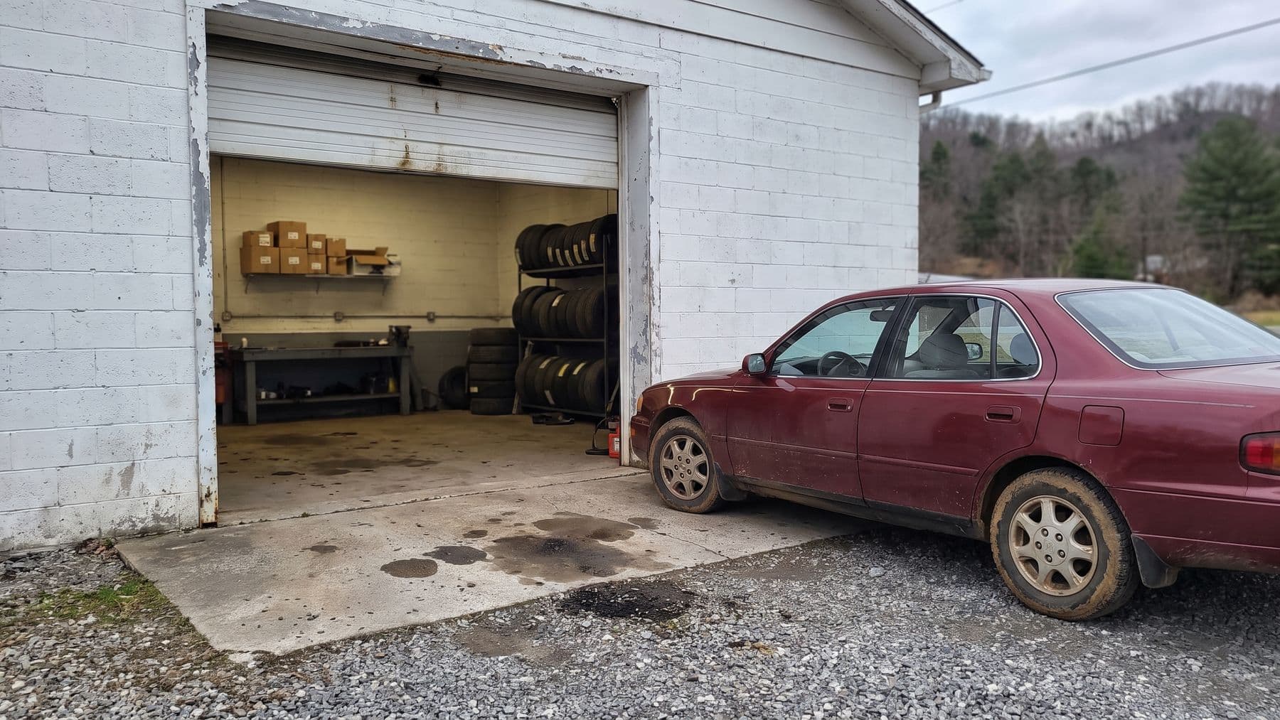 Illustration: a small white single-bay garage on a gravel lot in rural Tennessee, its roll-up door raised, wooded hills behind.